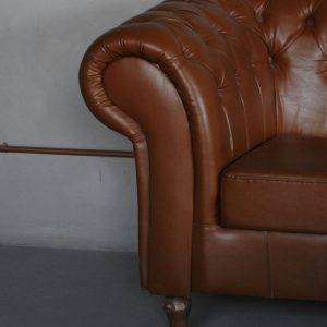 Close-up of a luxurious brown leather chesterfield sofa armrest indoors.